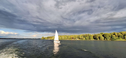 Segelboot auf der Müritz vor einer bewaldeten Uferlandschaft unter dunklen Wolken Segelboot auf der Müritz vor einer bewaldeten Uferlandschaft unter dunklen Wolken