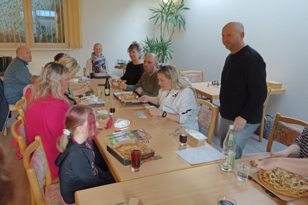 Teammitglieder sitzen um einen Tisch mit bestellten Pizzen in der Immanuel Begegnungsstätte Ecktannen im Heilbad Waren beim gemeinsamen Spieleabend für Mitarbeitende der Seniorenpflegeeinrichtung mit Tagespflegeangebot Immanuel Haus Ecktannen.