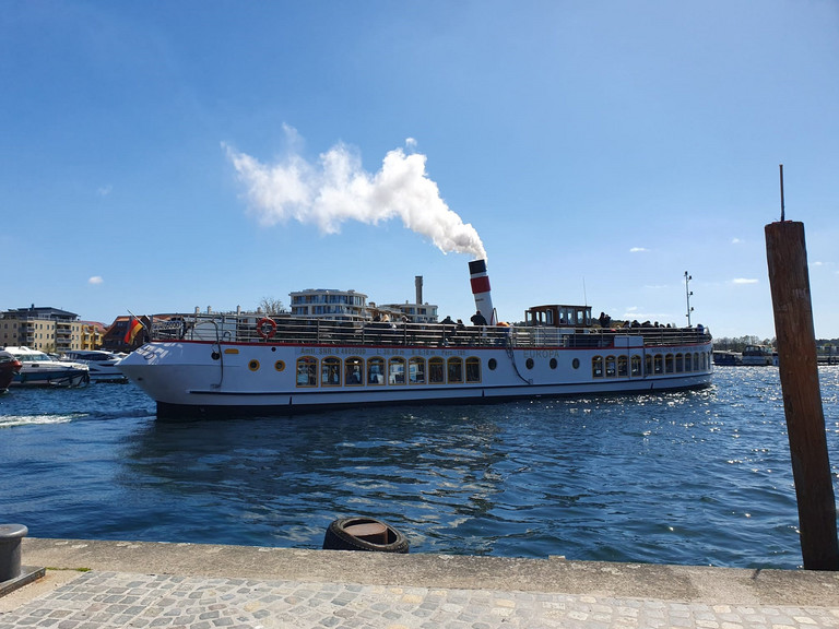 Ein Ausflugsschiff mit rauchendem Schornstein fährt von einem Kai ab