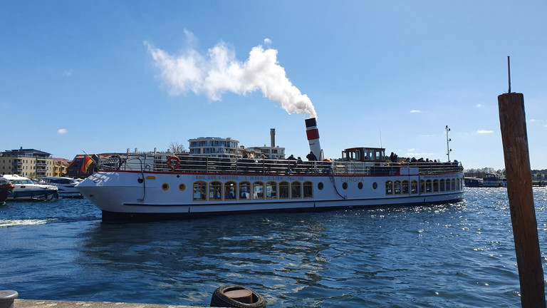 Ein Ausflugsschiff mit rauchendem Schornstein fährt von einem Kai ab