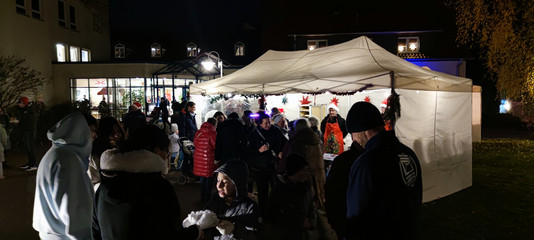 Besuchende des Weihnachtsmarktes des Immanuel Haus Ecktannen in der Dunkelheit vor erleuchteten Ständen Besuchende des Weihnachtsmarktes des Immanuel Haus Ecktannen in der Dunkelheit vor erleuchteten Ständen
