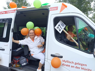 Eine Pflegekraft mit Lufballons sitzt im Transporter und blickt fröhlich in die Kamera beim Festumzug zum Jubiläums-Müritzfest mit Pflegekräften, Bewohnerinnen und Bewohnern aus dem Immanuel Haus Ecktannen